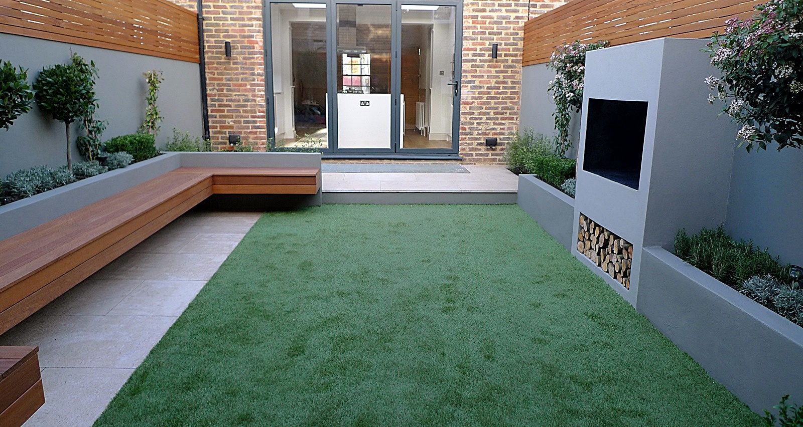 Modern garden designer London artificial grass hardwood seat fireplace
